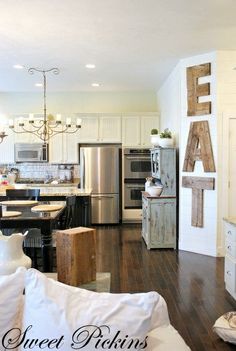 an open concept kitchen and living room with wood flooring, white painted walls and wooden letters on the wall