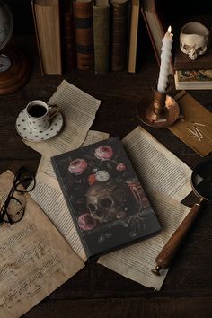 an open book sitting on top of a wooden table next to glasses and a candle