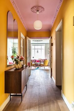 the hallway is painted bright yellow and has pink accents on the ceiling, along with wood flooring