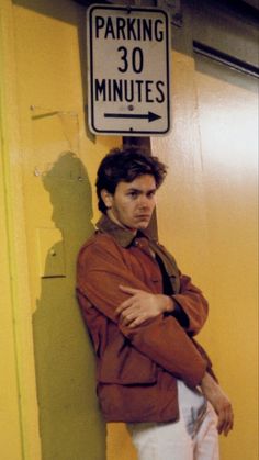 a man standing next to a parking sign on the side of a building with his arms crossed