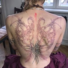 a woman with tattoos on her back sitting at a table