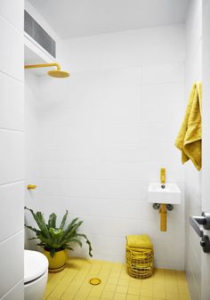 a bathroom with yellow accents and white tile on the walls, along with a potted plant