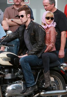 a man riding on the back of a motorcycle with a woman sitting on it's seat