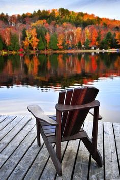 a chair sitting on top of a wooden dock next to a body of water with trees in the background