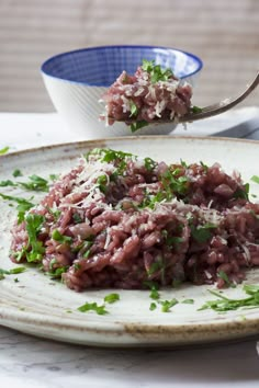 a white plate topped with meat and parsley next to a bowl of rice on a table