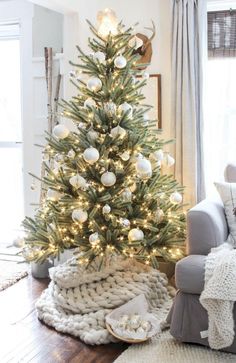 a christmas tree with white balls and lights in the corner of a cozy living room