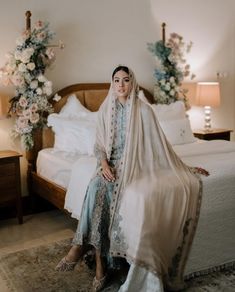 a woman sitting on top of a bed next to a white comforter and flowers