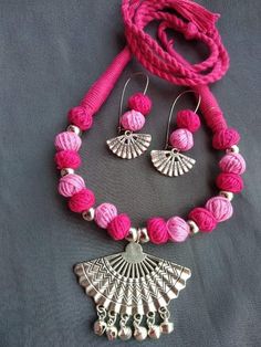 a pink necklace and earring set on a gray surface with silver beads, tassels