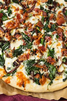 a pizza with bacon, spinach and cheese on it sitting on a piece of parchment paper