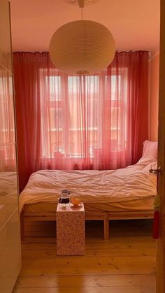 a bed sitting in a bedroom next to a window with red curtains on the windowsill