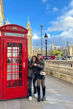 two women standing next to a red phone booth