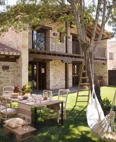 a hammock hanging from a tree in front of a house with picnic table and chairs