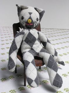 a gray and white cat stuffed animal sitting on top of a wooden chair with checkered fabric