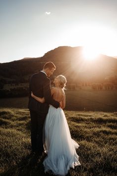 a bride and groom standing in the grass at sunset