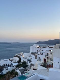 the sun is setting over some white buildings by the water in oia, greece