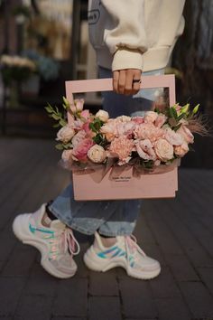 a person holding a pink box with flowers in it on the ground next to a brick walkway