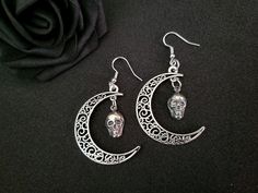 This beautiful earring set is handmade with mystique and wonder. Dainty skulls hang from an antique silver crescent moon, adding a touch of macabre elegance to any outfit. These earrings are a subtle statement piece and a fun conversation starter. Total length of the earrings with the hooks hang at approximately 3" inches. For longevity, it is recommended to steer clear of water and store in an air-tight container. The colors of the piece may vary slightly depending upon your monitor settings.  ------- Shipping: Ground Advantage (within the US) including tracking number Please visit http://www.etsy.com/shop/shaireproductions for more pieces. Thanks for looking!! © Design by Sherrie Thai of Shaireproductions.com. Copyrights are not transferrable with the sale of the item. Feel free to conne Gothic Jewelry With Moon Charm, Gothic Skull Earrings For Halloween, Gothic Nickel-free Jewelry For Festivals, Gothic Festival Jewelry With Moon Charm, Silver Moon-shaped Halloween Jewelry, Gothic Crescent Moon Charm Jewelry, Handmade Antique Silver Gothic Jewelry, Handmade Gothic Antique Silver Jewelry, Gothic Antique Silver Nickel-free Jewelry