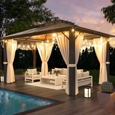 a gazebo with curtains and lights around it next to a pool at night time