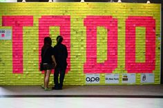 two people are standing in front of a wall covered with sticky notes that spell out words