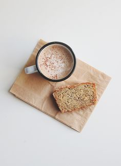 a piece of bread sitting on top of a napkin next to a cup of coffee