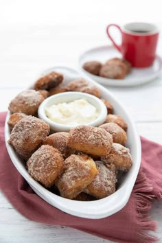 a bowl filled with donuts covered in powdered sugar next to a cup of yogurt