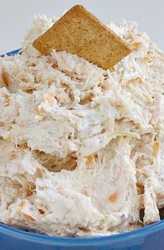 a blue bowl filled with chicken salad next to a cracker on top of it