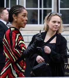 two women standing next to each other in front of a building and one is holding a purse