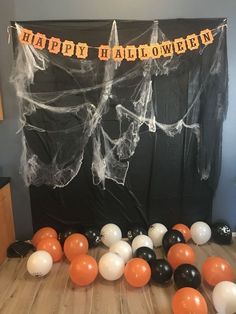 halloween decorations and balloons on the floor in front of a black backdrop with happy halloween written across it