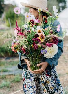 a woman holding a bouquet of flowers in her hands and wearing a hat on top of her head