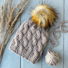 a knitted hat with a pom - pom sits next to some yarn