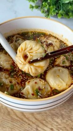 a bowl of soup with dumplings and chopsticks in it on a table