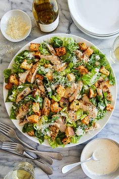 a salad with chicken and lettuce on a plate next to some wine glasses