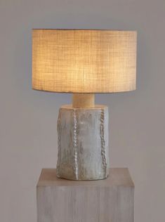 a table lamp sitting on top of a wooden block with a beige shade over it