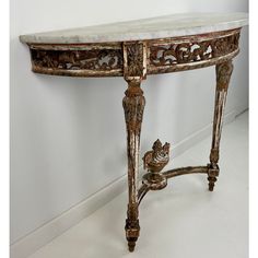 an antique console table with marble top and ornate carvings on the sides, against a white wall