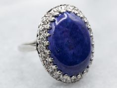 This white gold ring is a stunning example of modern elegance. It features a lapis centerpiece surrounded by a diamond halo, making it the perfect statement piece. Crafted with the highest quality materials, this ring will make a lasting addition to any jewelry collection.Metal: 14K White GoldGem: Lapis Gem Measurements: 13.1 x 18.4 mm, OvalAccents: 24 Single Cut Diamonds totaling .36 Carats, SI in Clarity, H-J in ColorRing Size: 7.25Marks: "14K" Stamped on the inside band Elegant Lapis Lazuli Ring With Polished Finish, Formal Lapis Lazuli Gemstone Ring, Oval Lapis Lazuli Rings For Formal Occasions, Formal Lapis Lazuli Oval Rings, Elegant Lapis Lazuli Rings For Formal Occasions, Elegant Formal Lapis Lazuli Rings, Silver Cabochon Platinum Rings, Silver Platinum Rings With Cabochon, Platinum Silver Rings With Cabochon