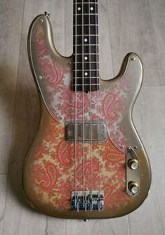 an electric bass guitar sitting on top of a hard wood floor covered in paisley fabric