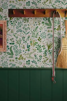 a broom is hanging on the wall next to a green painted wall with flowers and leaves