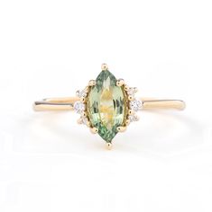 an oval cut green and white diamond ring with two diamonds on each side, set in yellow gold