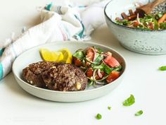 two bowls filled with meat and vegetables on top of a white tablecloth next to a wooden spoon