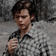 a young man holding a stick in his hand and looking at the camera while wearing a plaid shirt