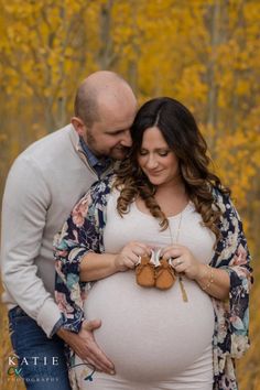 a pregnant woman holding her husband's belly while they stand in front of yellow trees