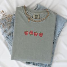 Welcome the sunny days with our delightful Summer Strawberry Embroidered T-Shirt! Made from 100% cotton, this t-shirt is not only comfortable but also perfect for staying cool during warm weather. Available in sizes S to 2XL and nine vibrant colors including Banana, Bay, Blossom, Butter, Chalky Mint, Chambray, Ivory, Orchid, and Peachy, there's a shade to suit every style.The standout feature of this t-shirt is the charming summer fruit-inspired design, showcasing four intricately embroidered strawberries on the center chest. Whether you're heading to a picnic, beach outing, or simply enjoying a leisurely day, this t-shirt adds a touch of sweetness to your summer wardrobe.Please note that colors may vary slightly due to monitor settings. For accurate sizing, refer to the size charts provid Trendy Embroidered Tops For Everyday, Summer Cotton T-shirt For Everyday, Cute Summer Tops With Embroidered Graphics, Cute Everyday Cotton T-shirt, Casual Embroidered Tops For Everyday, Cute Cotton Tops With Embroidered Text, Cute Organic Cotton T-shirt For Everyday, Spring Embroidered Top For Everyday Wear, Embroidered Tops For Everyday Spring Wear