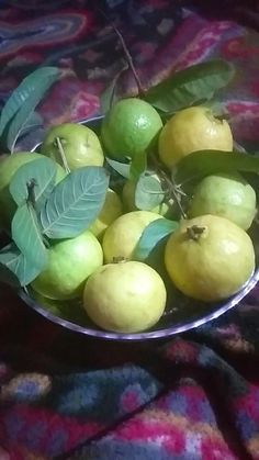 a metal bowl filled with green and yellow fruit on a tablecloth covered surface,