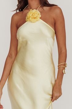 a woman wearing a white dress with a yellow rose on the shoulder and gold bracelets