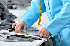 a person measuring the length of clothes on a table with a tape measure in front of them