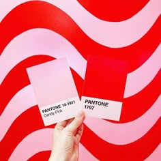 someone holding up two matching pantone cards in front of a red and white wall