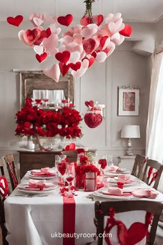 valentine's day table setting with red and pink hearts hanging from the ceiling over it