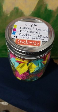 a jar filled with lots of different colored paper clips on top of a blue table