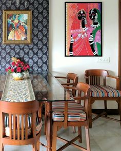 a dining room table with chairs and paintings on the wall behind it, along with two vases filled with flowers