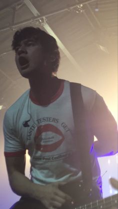 a man with a guitar standing in front of a microphone and some lights behind him